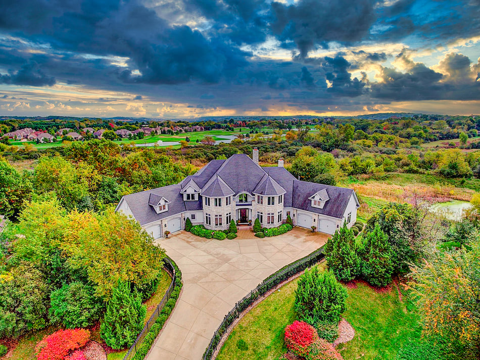 Professional real estate aerial drone photography and videography sample showing large lucury home surrounded by green lush landscaping and a sunset at twilight hours with clouds